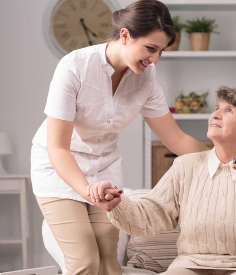 A carer helping an older lady stand from her chair at home